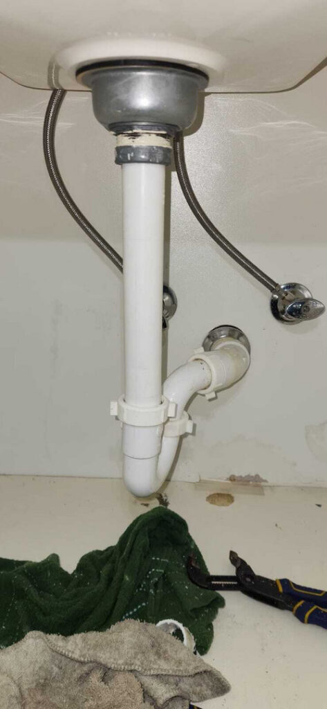plumbing installation under a sink with white pipes and metal connections alongside towels and a wrench in the area