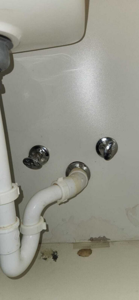 plumbing installation with metal valves and white pipes visible on a beige wall with some stains and discoloration