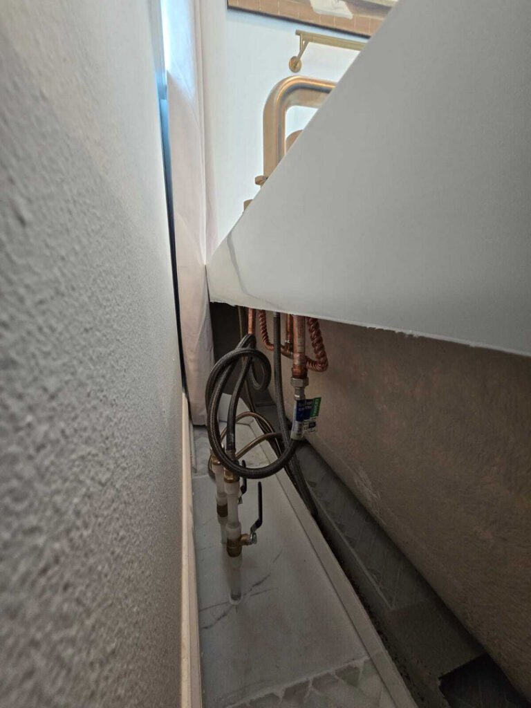 plumbing installation with visible pipes and fittings located under a tub in a confined space