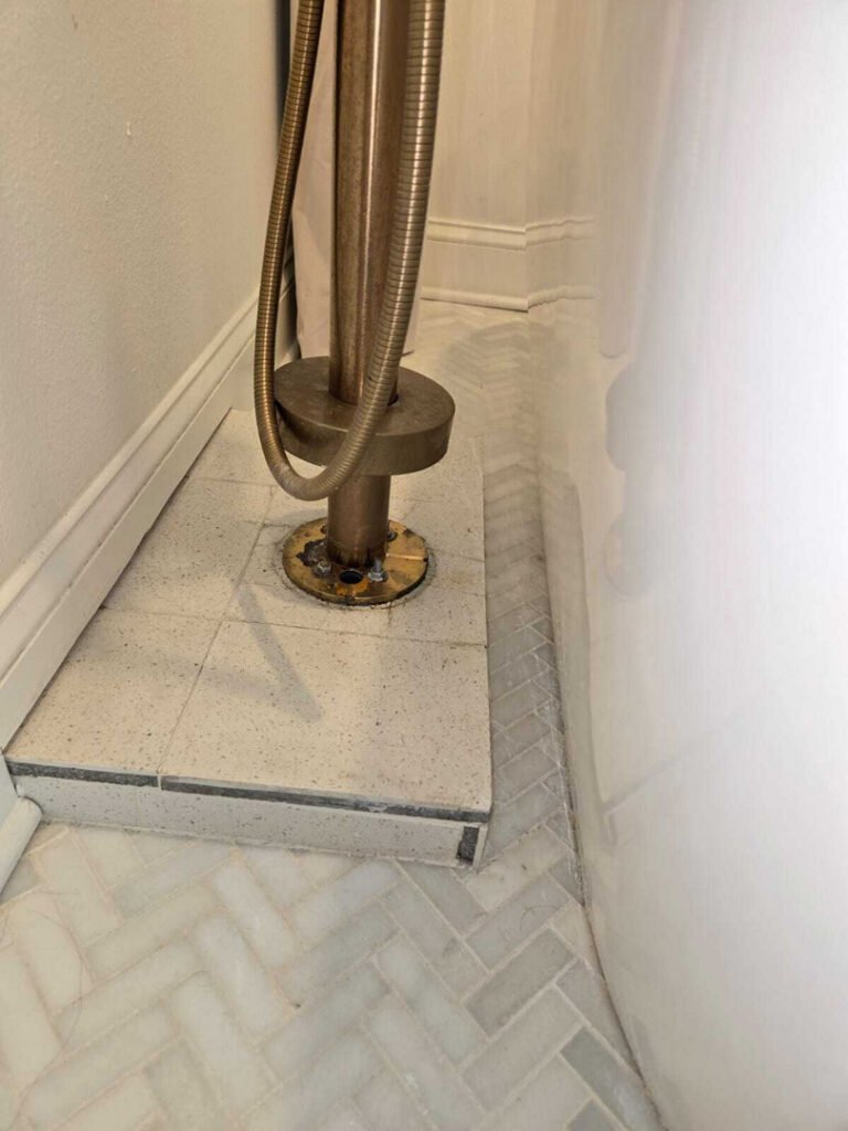 plumbing repair involving a metallic pipe with hoses connected to a drain area on tiled flooring