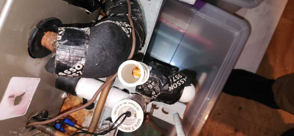plumbing repair involving pipes taped with black insulation tape showing potential leaks and connectors on a basement floor