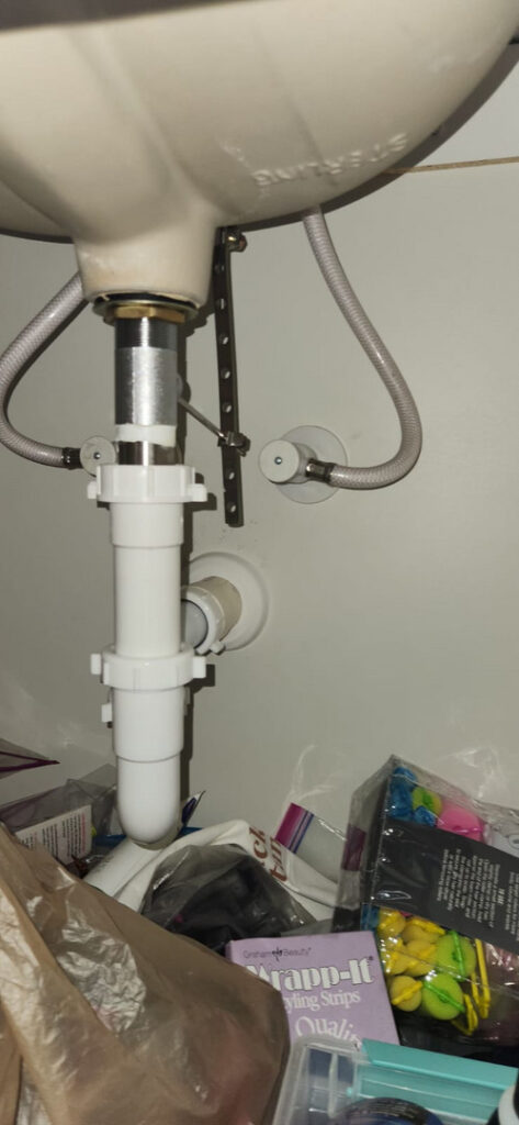 plumbing repair underneath a sink with pipes and connections visible among cluttered items