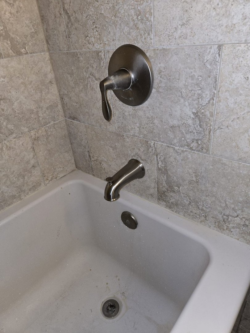 plumbing service inspecting or repairing a bathtub faucet and handle in a tiled bathroom