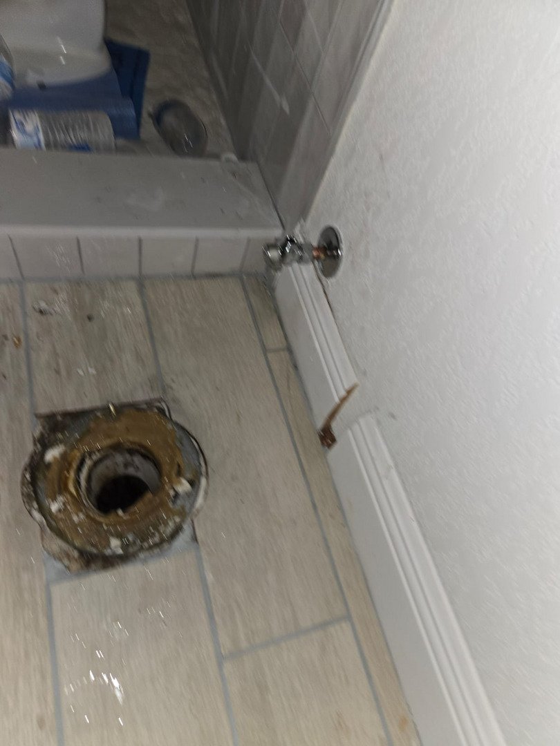 plumbing work being done with a visible toilet flange and plumbing fittings on tiled flooring