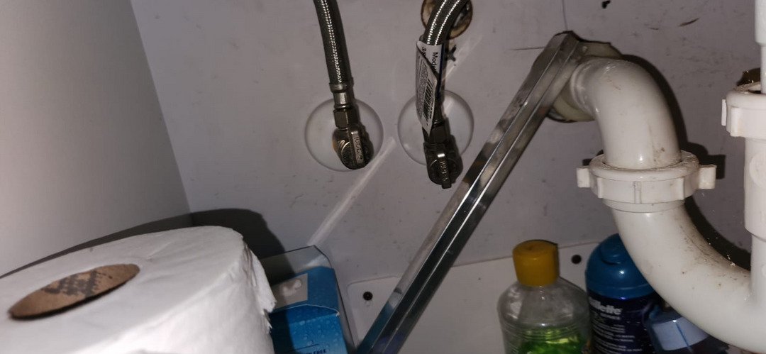 plumbing work on water supply lines near a toilet with visible plumbing components and cleaning supplies in the background