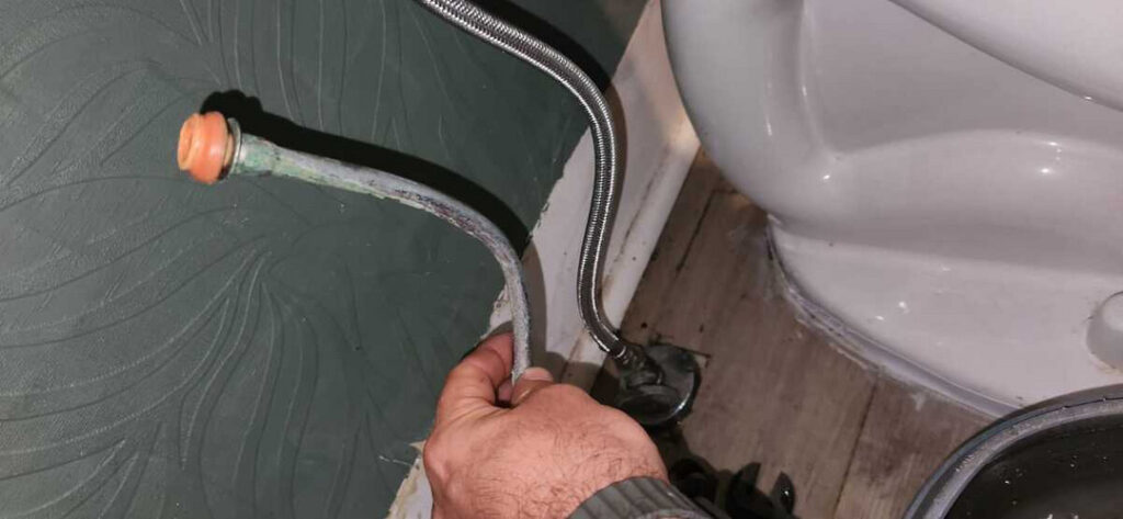 removing and inspecting plumbing connections near a toilet in preparation for repair or maintenance services