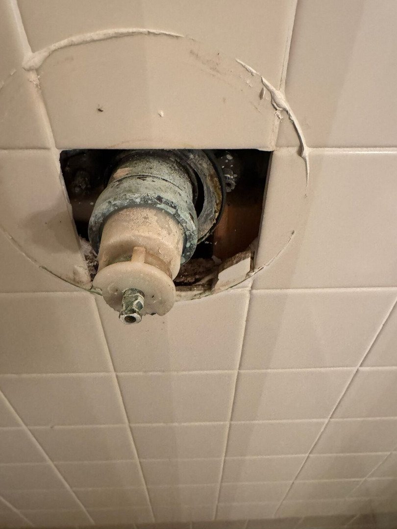 repairing a damaged shower valve assembly in a tiled wall revealing exposed plumbing components and potential leaks