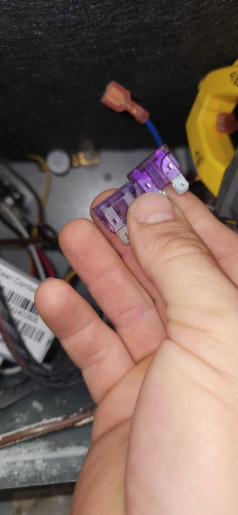 replacing a fuse in an electrical panel with purple fuses in a hand near wiring and components