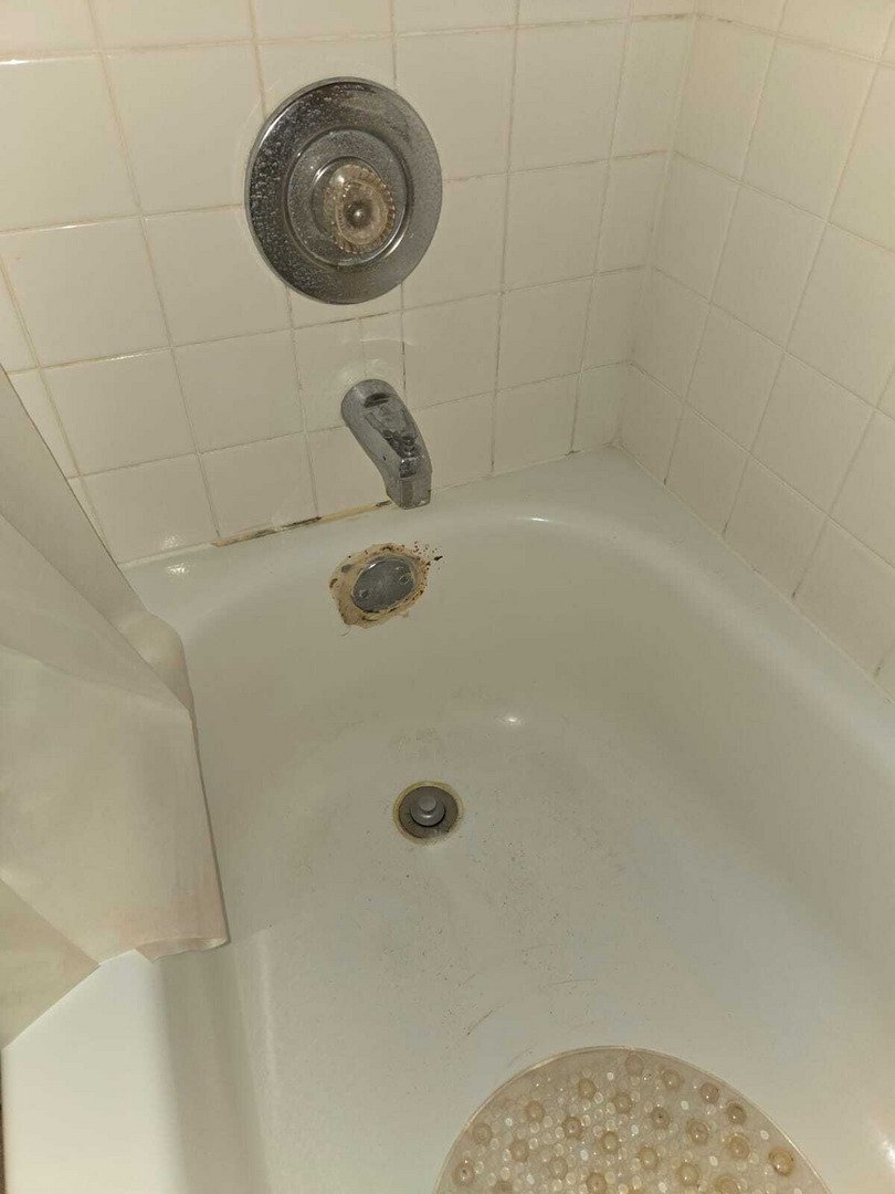 stained bathtub with visible rust and grime around faucet and drain area indicative of a plumbing repair or cleaning service needed