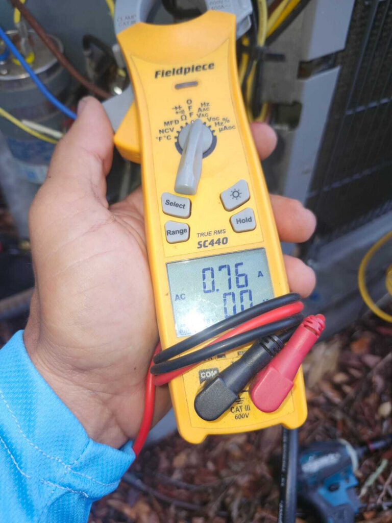 technician using a multimeter to measure electrical current near HVAC equipment