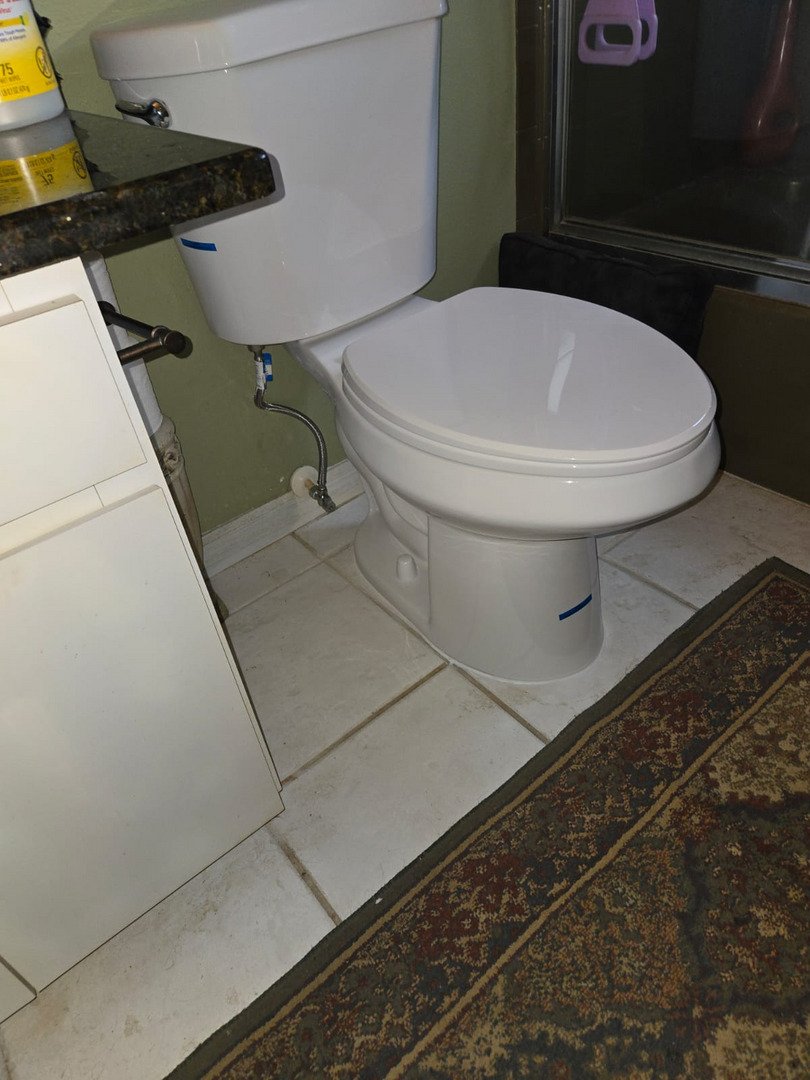 toilet installation in a bathroom with white tiles and a dark rug nearby