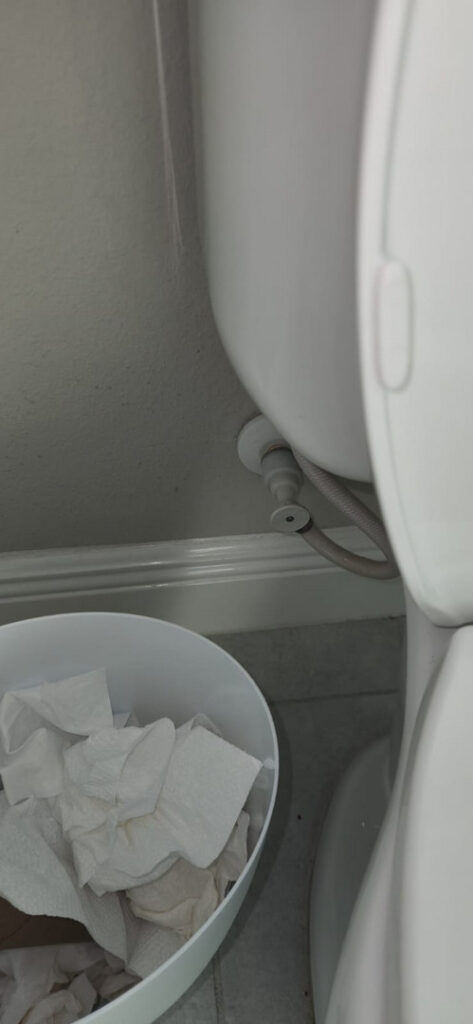 toilet maintenance with a visible wastebasket for used paper products and plumbing connections behind the toilet