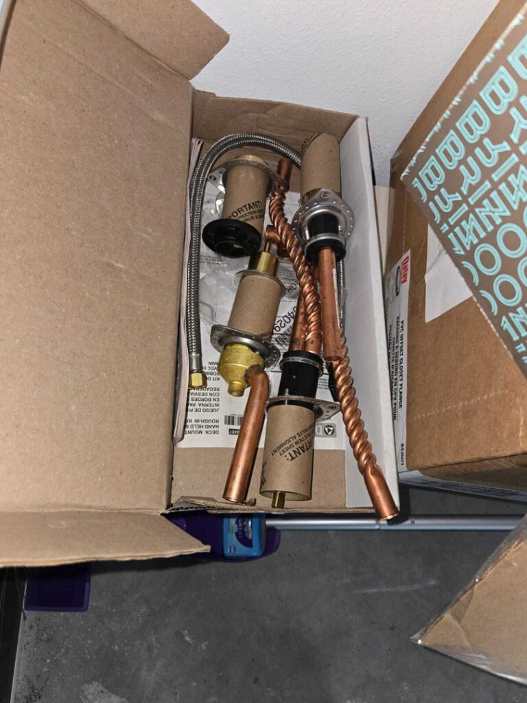 various plumbing parts including valves and copper tubing organized in a box with paperwork in the background