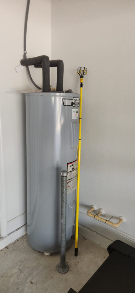 water heater installation with a yellow tool for plumbing adjustments and visible pipes against a garage wall