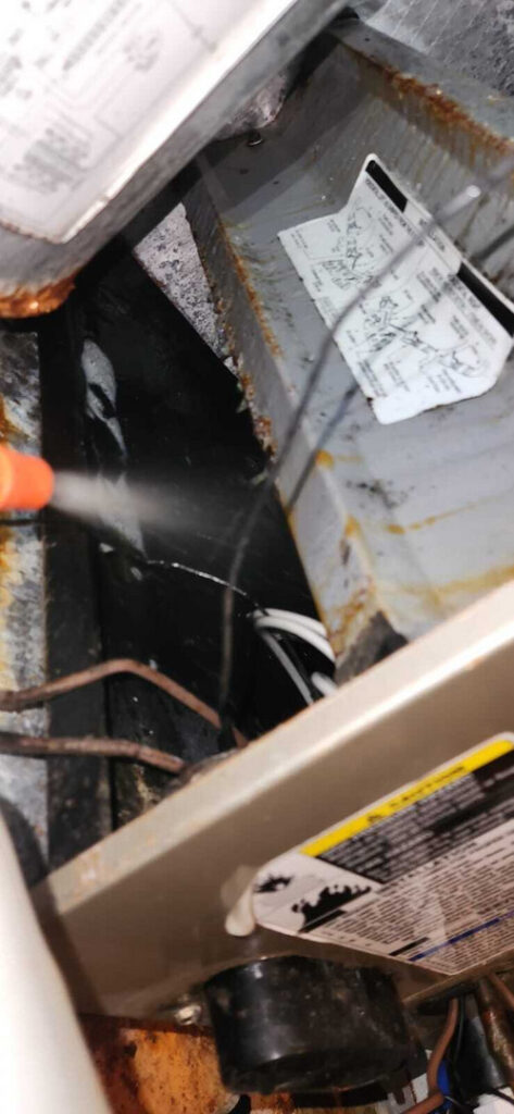 water is being sprayed likely for cleaning or maintenance on a heating or cooling system component