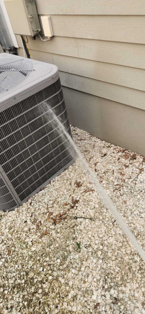 water is being sprayed onto a cooling unit likely for cleaning or maintenance purposes near a gravel area