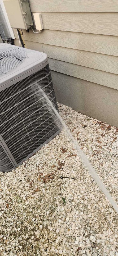 water is being sprayed onto a cooling unit likely for cleaning or maintenance purposes near a gravel area