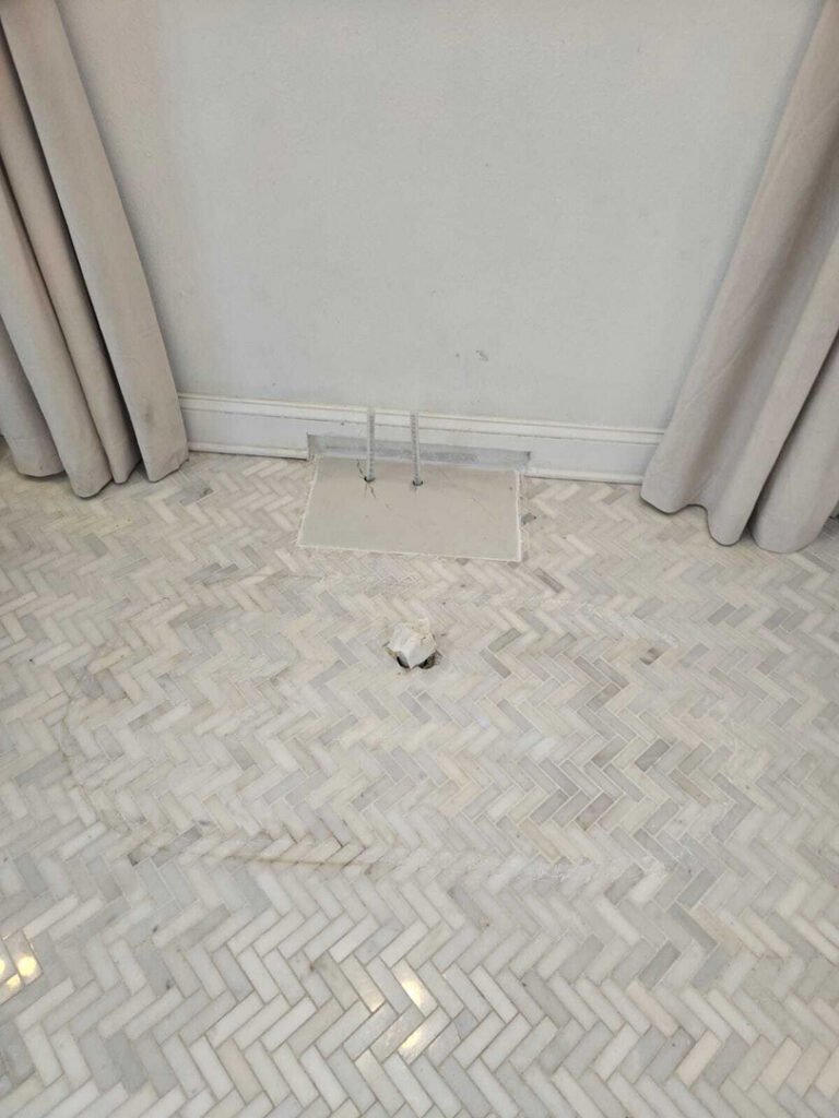 white marble floor with a vent cover and a small object nearby curtains hanging on the side of the wall