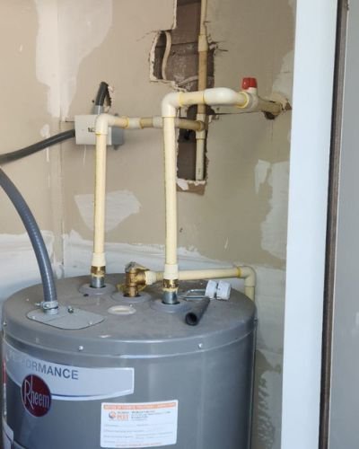 water heater installation with visible plumbing connections and energy guide label in a partially finished wall setting