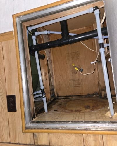 plumbing repair visible with black and white pipes inside a wooden enclosure possibly addressing a leak or drainage issue