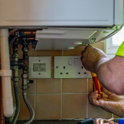 Plumber Working On Boiler Installation In Kitchen Utilities