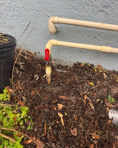 water line installation with pvc pipes and a shutoff valve on a grassy soil area near a house wall